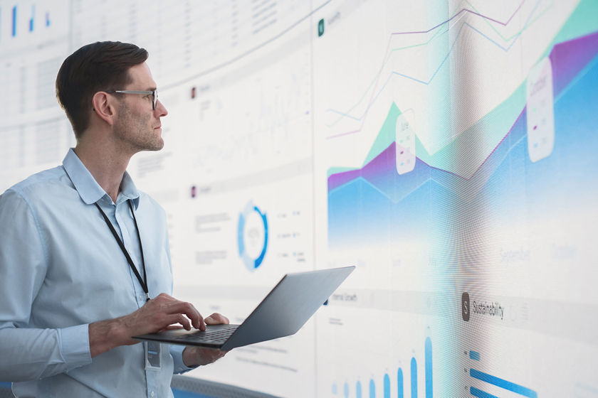 Worker Holding Laptop Reviewing Data Screens 