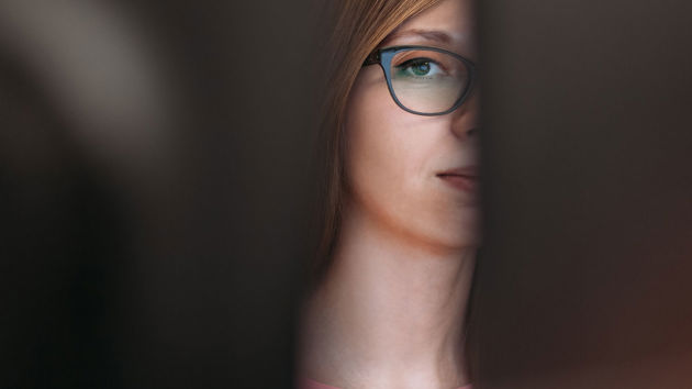 Woman Peering Between Two Computer Monitors 