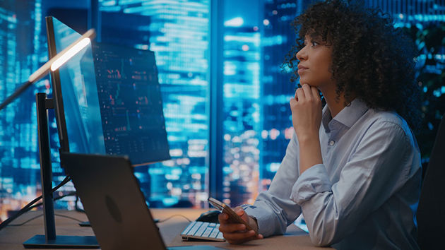 Woman Reviewing Data On Computer Monitors 