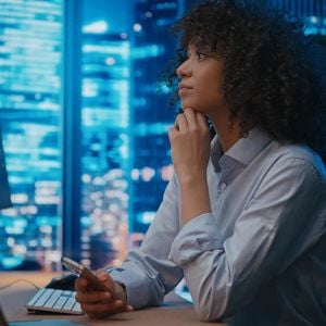 Woman Looking At Computer Holding Phone 