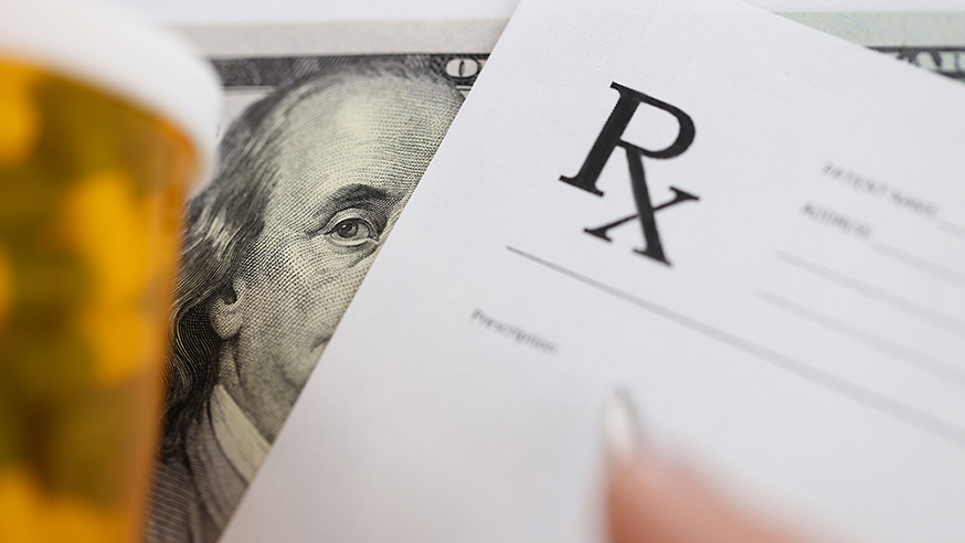A prescription pad and pill bottle in front of a one hundred dollar bill.