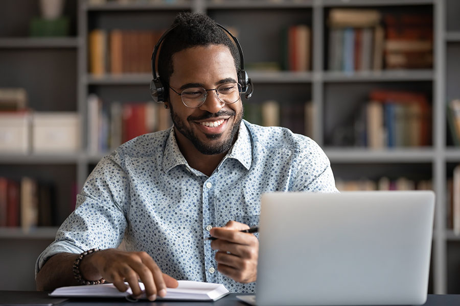 man-wearing-headphones-smiling-at-laptop-while-writing