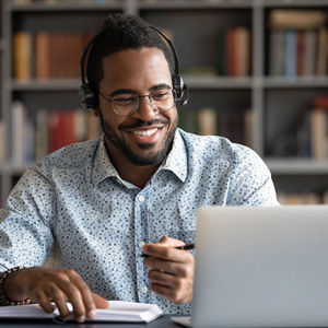 Man Wearing Headphones Smiling At Laptop While Writing 