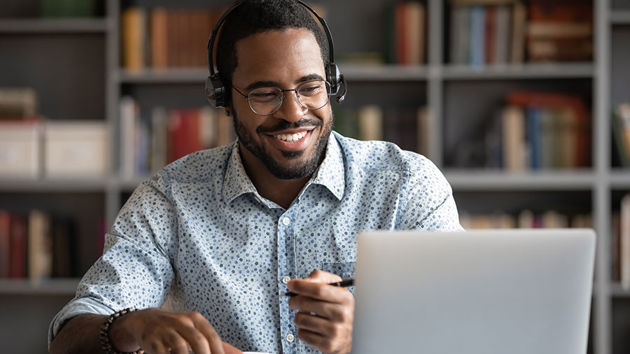 Man Wearing Headphones Smiling At Laptop While Writing 
